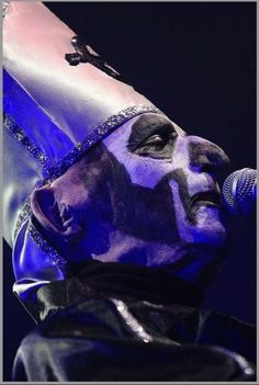 a man with his face painted in blue and white, holding a microphone up to his mouth