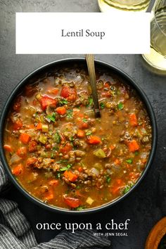 a bowl of lentil soup on a table with a glass of wine in the background