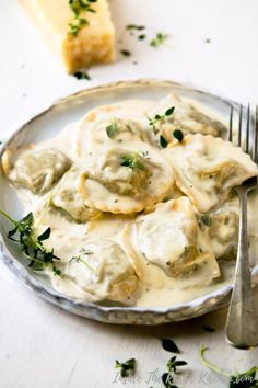 a white plate topped with ravioli next to a slice of bread and a fork