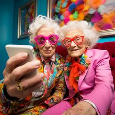 two older women sitting on a red couch looking at a cell phone while wearing pink glasses