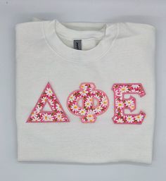 a white t - shirt with the word aoe spelled in pink letters and daisies