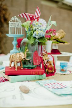 a table topped with vases filled with flowers and figurines on top of books