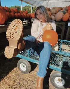 a woman sitting on top of a blue wagon holding a pumpkin and wearing brown boots