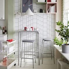 two stools and a table in a room with white tiles on the wall behind them