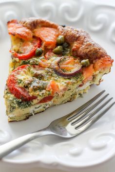 a slice of quiche with tomatoes and capers on a plate next to a fork