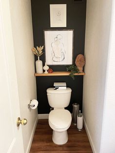 a white toilet sitting inside of a bathroom next to a wooden floor and framed artwork