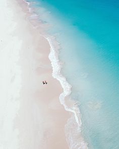 an aerial view of two people walking on the beach