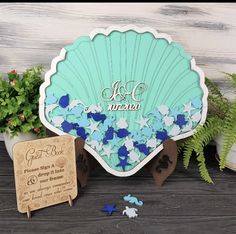 a wooden sign with blue and white confetti on it next to some potted plants