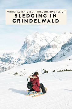 a person sitting in the snow on a sled with mountains in the back ground