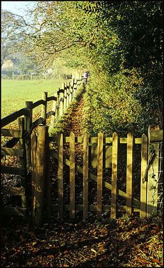 a wooden fence with a person walking on it in the distance near a grassy field