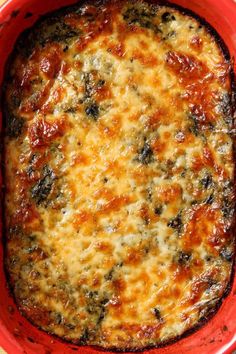 a red casserole dish with cheese and spinach on the top in a bowl