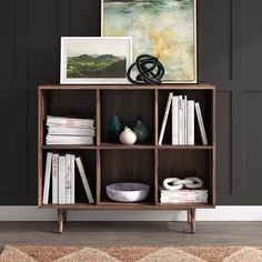 a bookcase with books and pictures on top of it in front of a black wall