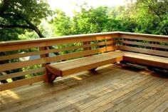 two wooden benches sitting on top of a wooden deck next to trees and bushes in the background