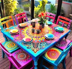 a colorful table and chairs on a deck with flowers in vases sitting at the center