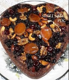 a heart - shaped cake with nuts and raisins on top sits on a plate