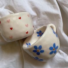 two white cups with blue and red flowers on them are sitting on a bed sheet