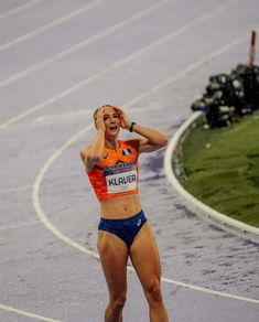 a female athlete in an orange top and blue shorts is on the track with her hands behind her head