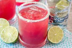 two glasses filled with red liquid and limes next to each other on a table