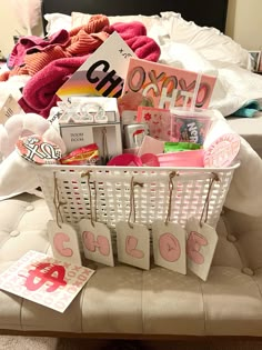 a white basket filled with lots of items on top of a bed next to a pile of blankets