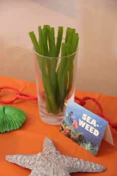 there is a starfish and some seaweed in a glass on an orange table