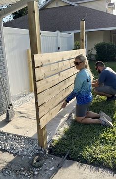 two people laying on the ground next to a wooden fence and some grass in front of a house