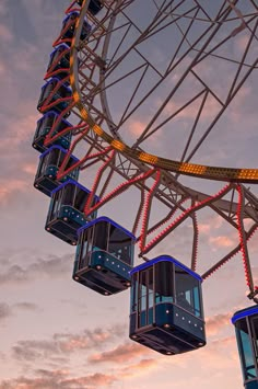 a ferris wheel with blue and red seats in front of a cloudy sky at dusk