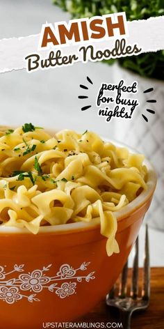 an orange bowl filled with pasta on top of a wooden table next to a fork and knife