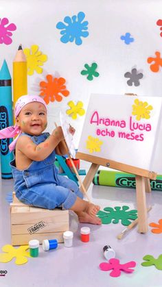 a baby sitting in front of a sign with crayons and paint on it