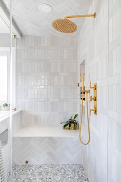 a white tiled bathroom with gold fixtures and an open shower head on the wall next to a window