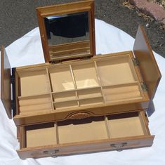 an open wooden jewelry box sitting on top of a white cloth covered table next to a mirror