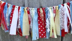 a bunch of ribbons are hanging from a line on a wooden fence with the colors of red, white, and blue