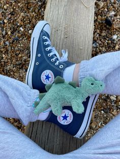 someone wearing blue converse shoes with a green dinosaur stuffed animal