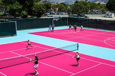 a group of people playing tennis on a pink and blue court with mountains in the background