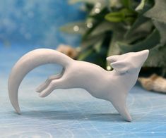 a small white cat figurine sitting on top of a table next to a potted plant