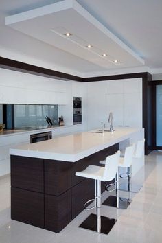 a modern kitchen with white counter tops and bar stools next to an island in the middle