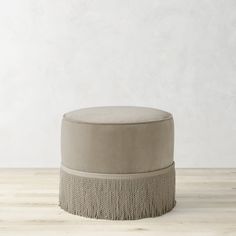 a round ottoman sitting on top of a hard wood floor next to a white wall