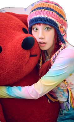 a woman hugging a large red teddy bear wearing a knitted hat and colorful scarf