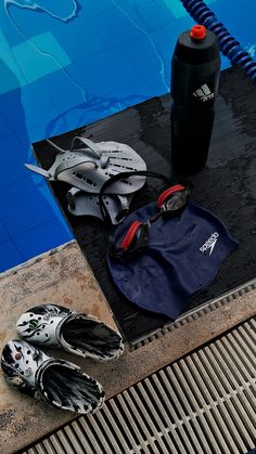 a pair of swimming shoes, water bottle and wetsuit next to a swimming pool