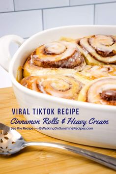 a white dish filled with cinnamon rolls on top of a wooden table