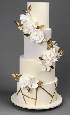 a three tiered cake with white flowers and gold leaves