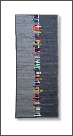 a quilted wall hanging on the side of a white wall with black and grey stripes