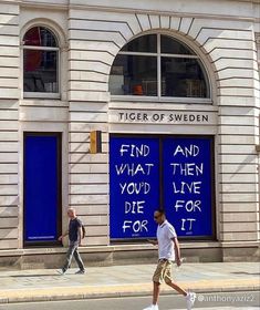 two men walking down the street in front of a building with blue doors and graffiti on it