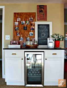 a wine cooler in the middle of a room with pictures on the wall above it