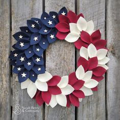 a patriotic wreath made out of red, white and blue paper flowers sitting on top of a wooden fence