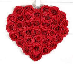 a heart made out of red roses sitting on top of a white wooden table next to a wall