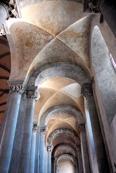 the inside of an old building with columns and arches on either side, looking up at the ceiling