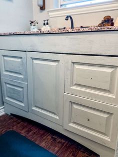 a bathroom vanity with white cabinets and marble counter tops, along with a blue rug on the floor