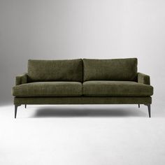 a green couch sitting on top of a white floor next to a gray wall in an empty room