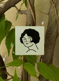 a piece of paper with a drawing of a woman's face hanging from a tree