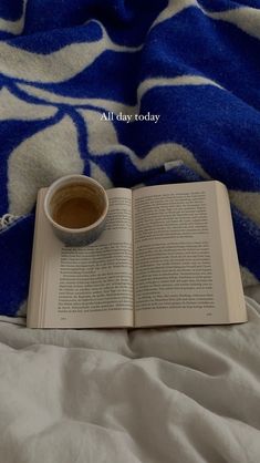 an open book with a cup of coffee sitting on top of it next to a blue and white blanket